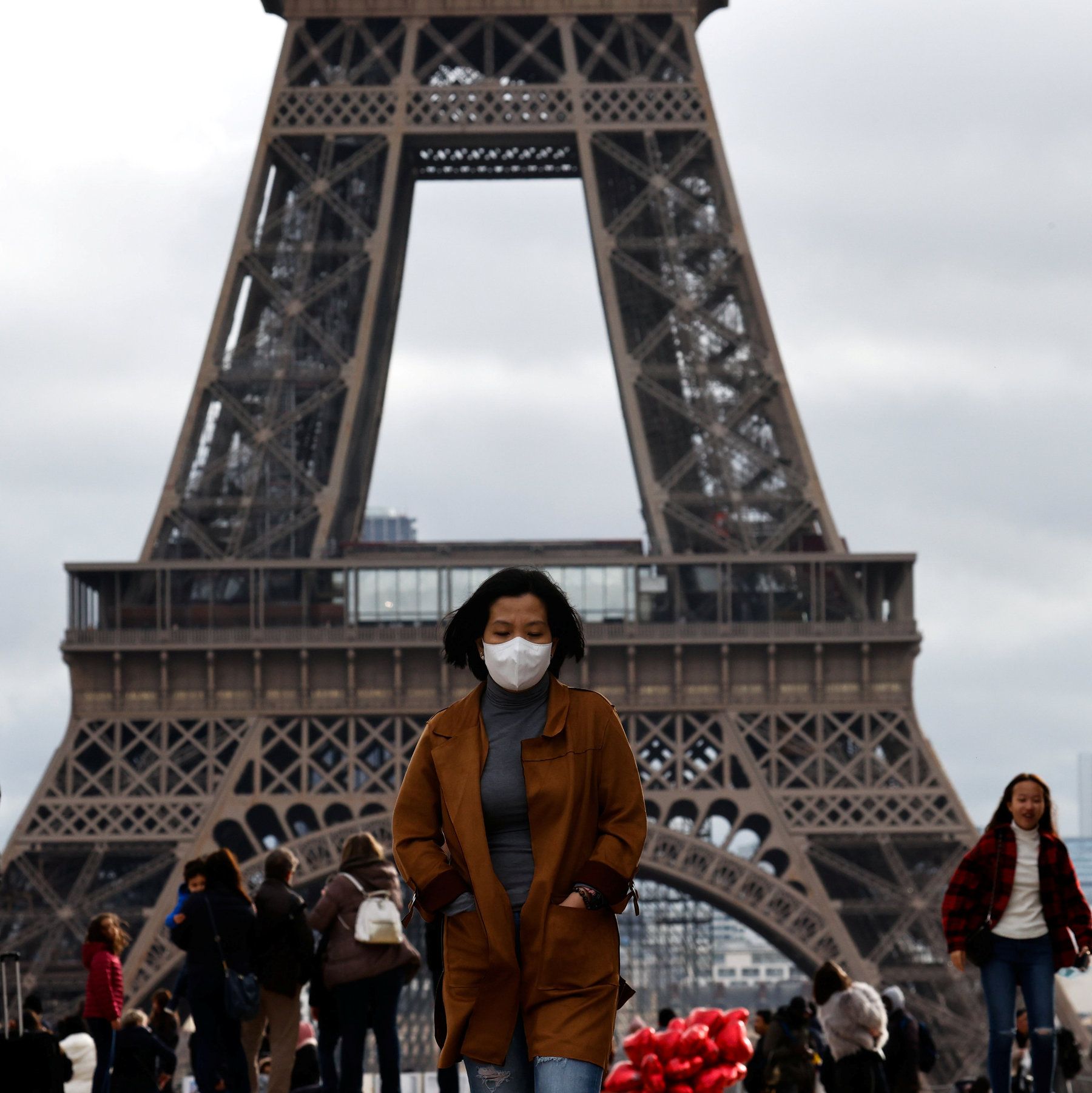 Uma mulher usando uma máscara em frente à Torre Eifell.