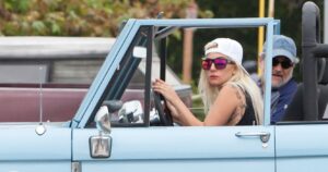 Lady Gaga driving a powder-blue Bronco while wearing sunglasses and a backward baseball cap